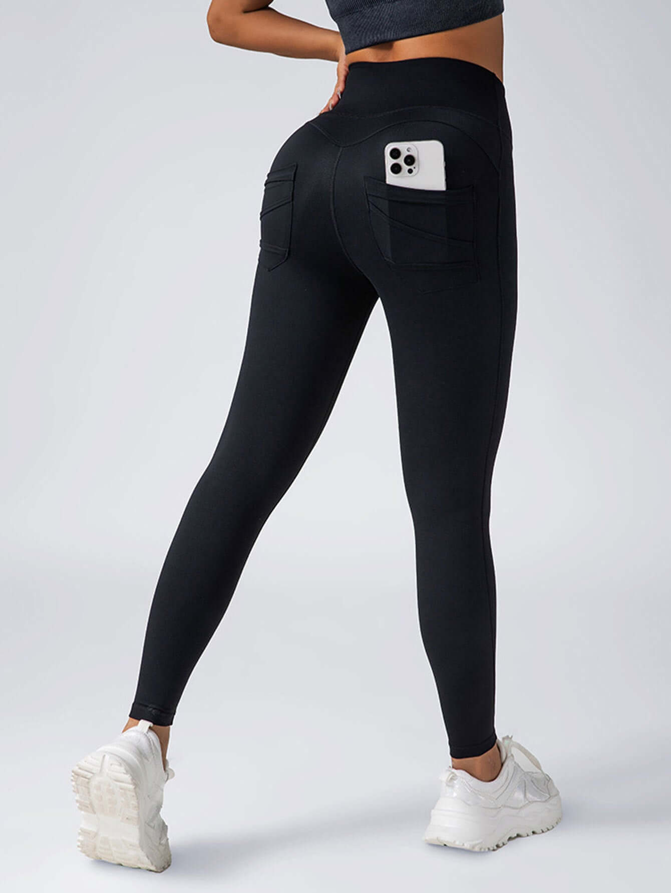 Womens black high-waisted yoga leggings with back pockets, featuring 4-way stretch and phone tucked in.