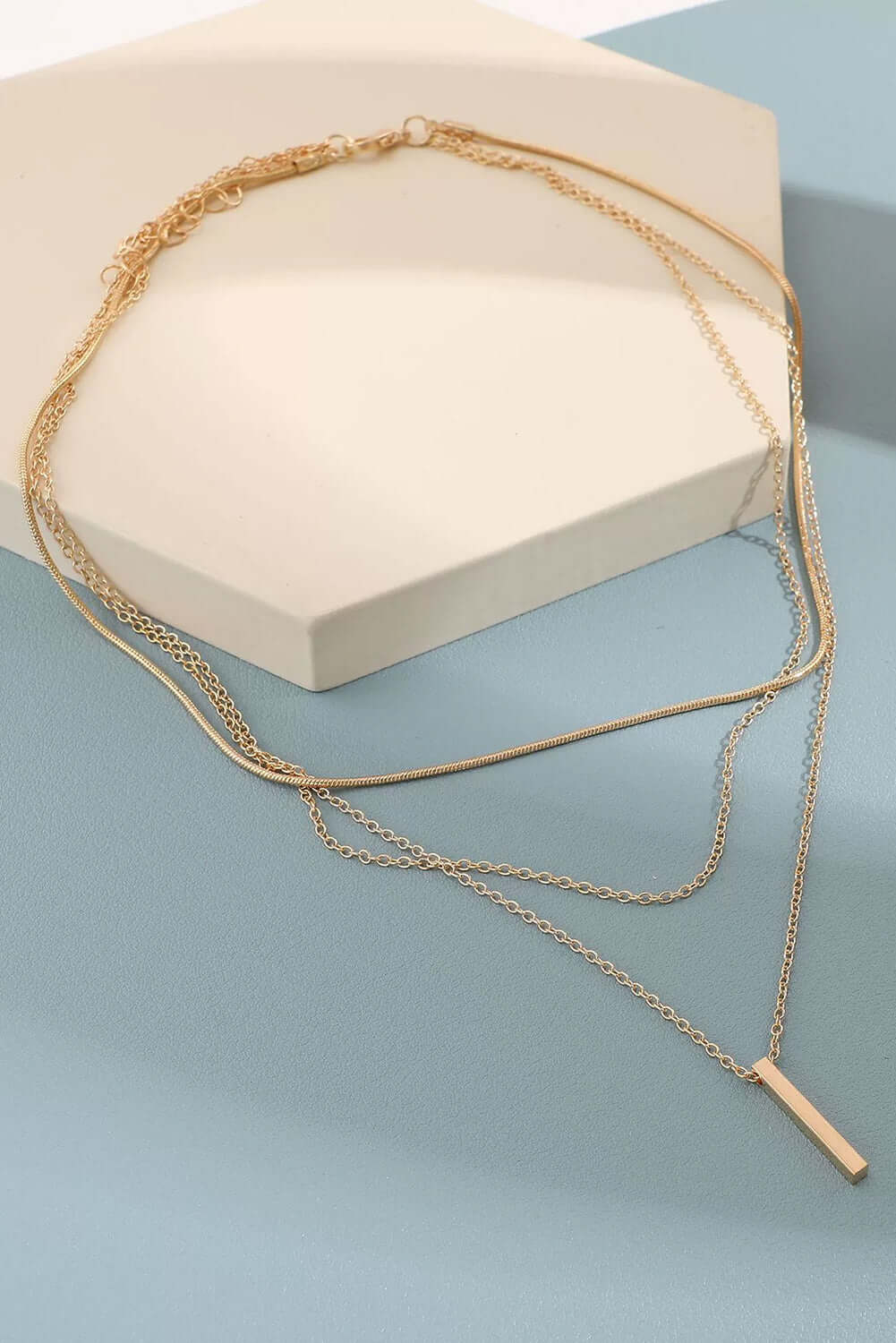 Elegant gold bar pendant layered necklace with adjustable chain on a geometric display.