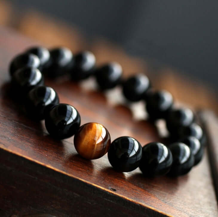 Natural black onyx bracelet with tiger eye stone bead on wooden surface.