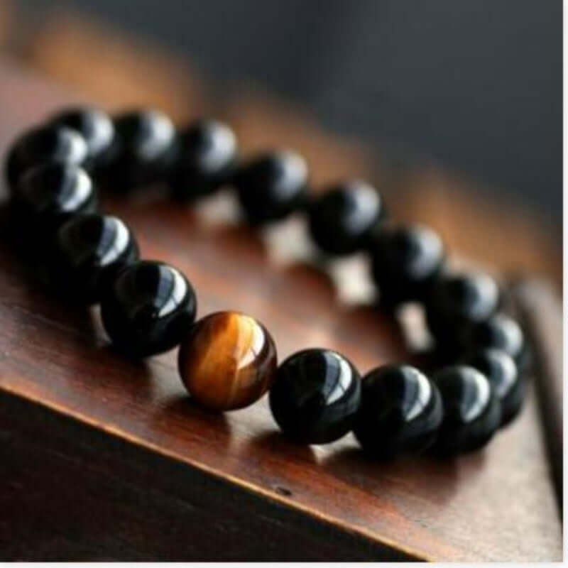 Natural black onyx and tiger eye energy bracelet on wooden surface.