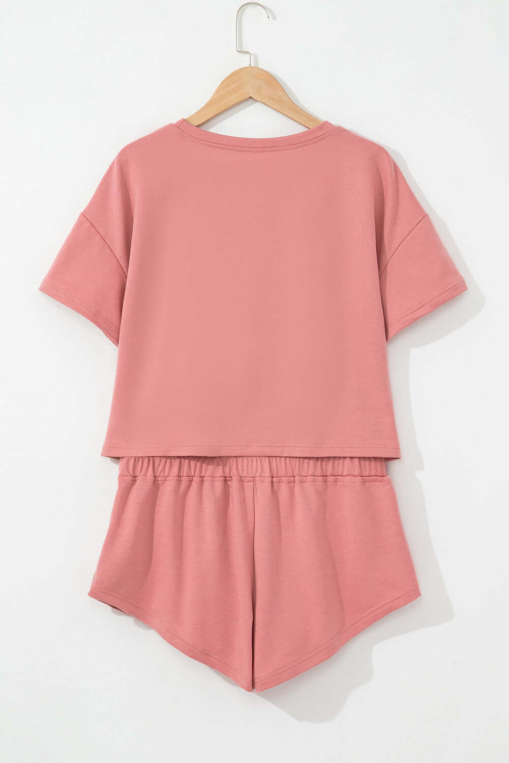 Blossom cropped tee and ruffle high waist skort set in pink hanging on a wooden hanger, showcasing back view.