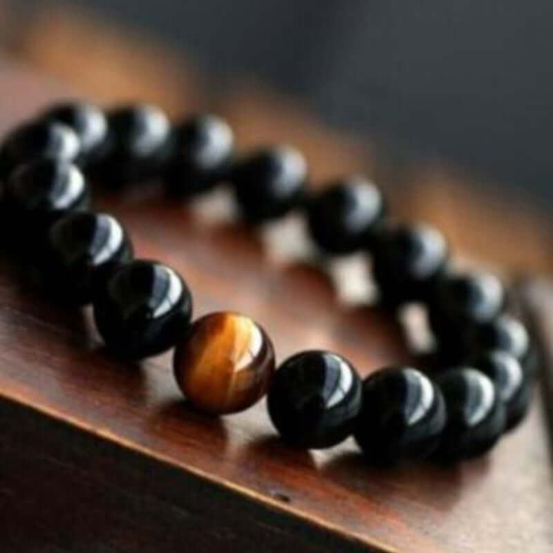 Natural black onyx and tiger eye stone energy bracelet on wood surface.