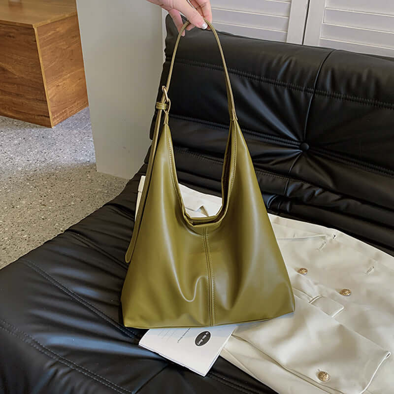 Large capacity green commuter tote for women on black leather couch.