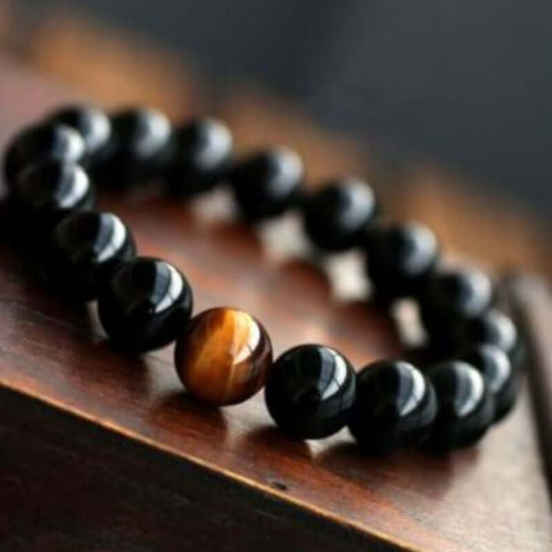 Natural black onyx and tiger eye stone energy bracelet on wooden surface.