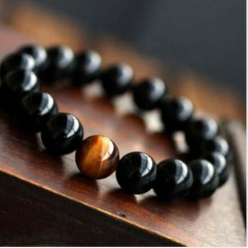 Natural black onyx and tiger eye stone energy bracelet on a wooden surface.