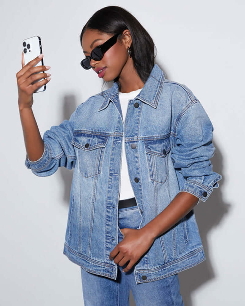 Woman in denim jacket and jeans taking a selfie, showcasing casual fashion.