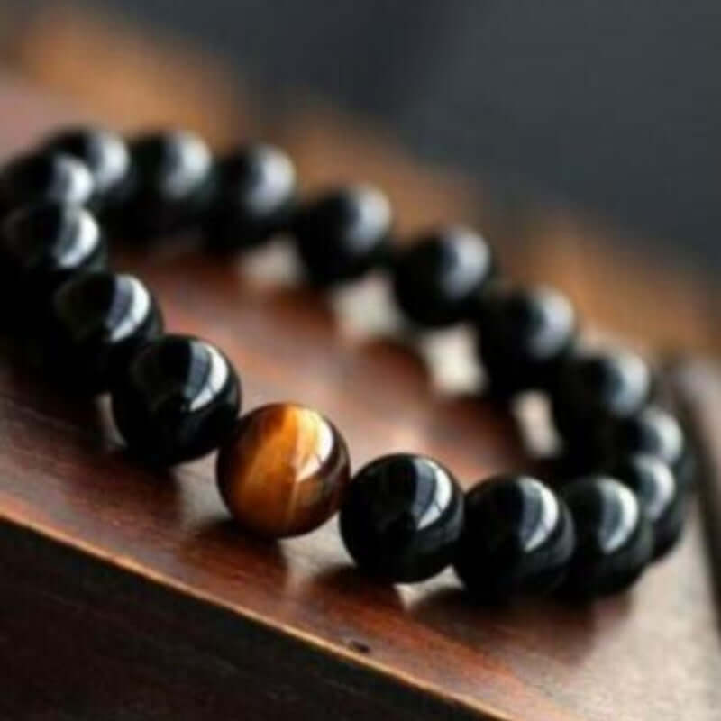 Natural black onyx and tiger eye stone energy bracelet on a wooden surface.