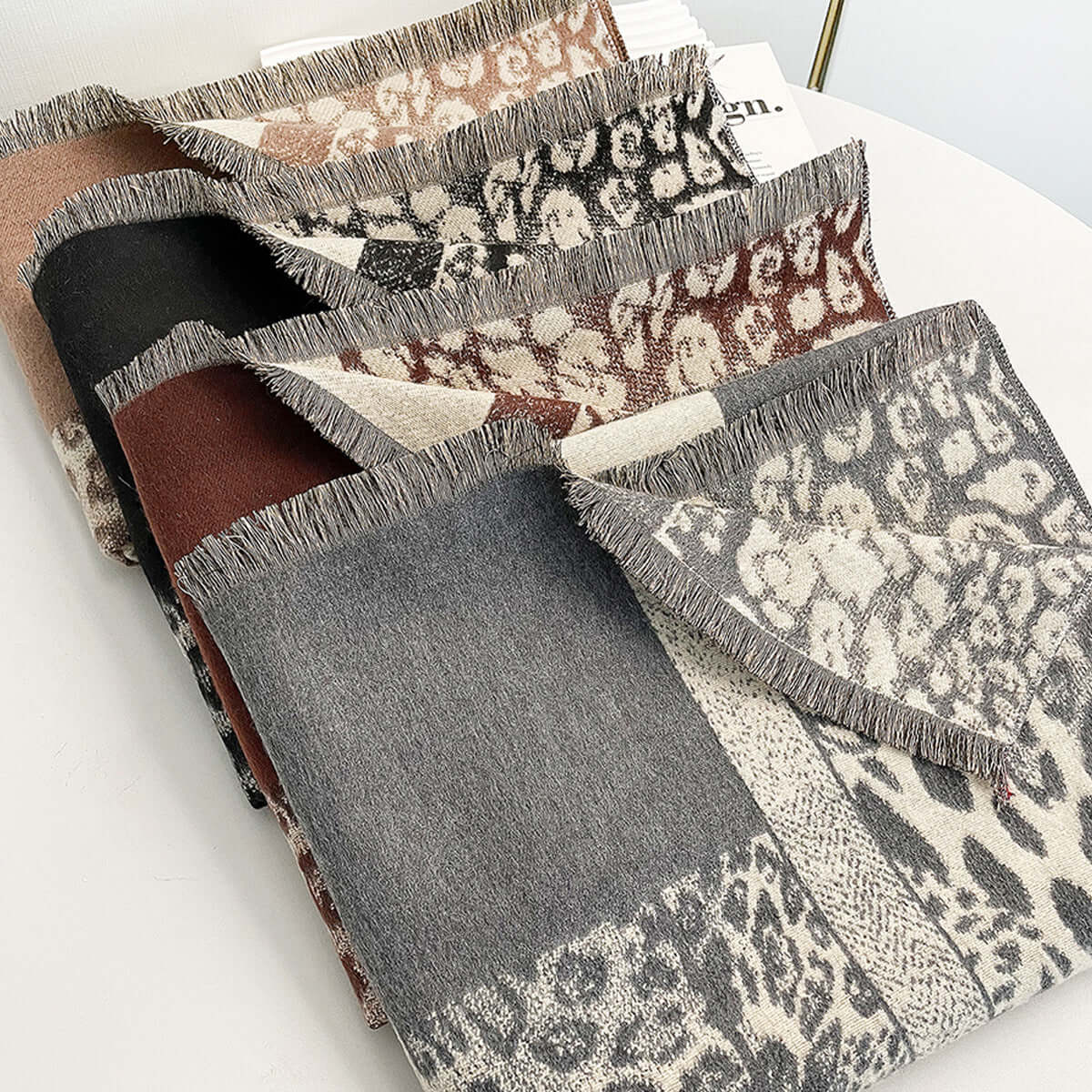 Autumn and winter color-blocking leopard print scarf in black, gray, light brown, and dark brown, imitation cashmere fabric, displayed folded on a table.