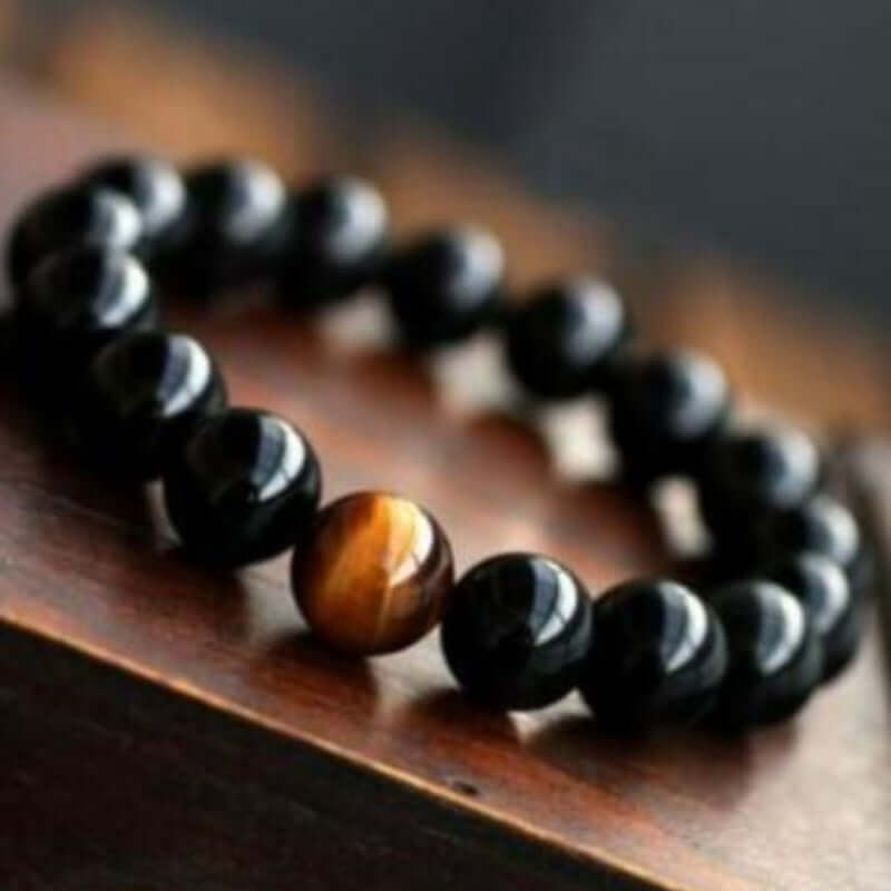 Natural black onyx and tiger eye stone energy bracelet on a wooden surface.