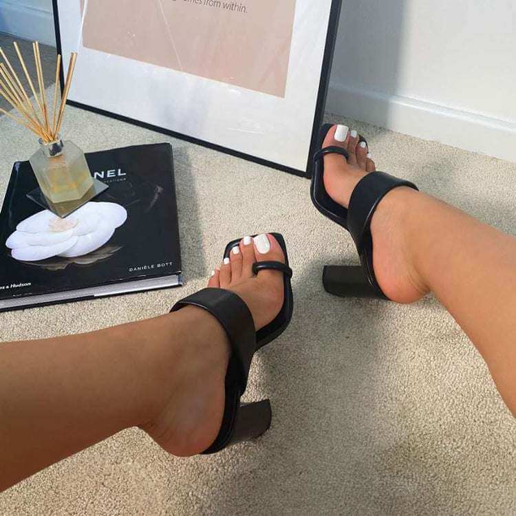 Casual black thick heel sandals with square toe and buckle strap, worn by a woman, resting on a beige carpet.