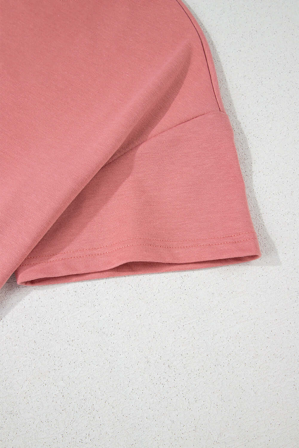 Close-up of the sleeve and hem of a pink cropped tee, showcasing the soft fabric and clean finish.