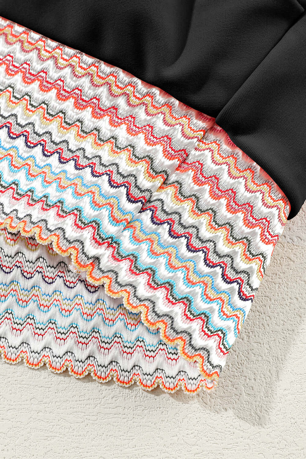 Close-up of vibrant zigzag patterned fabric in colorful stripes, featured in a chic black bikini design.