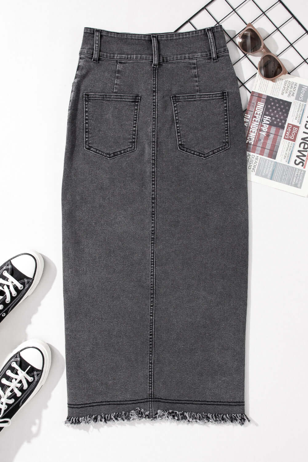 Black midi denim skirt with raw edge hem, buttoned closure, and side slits, styled with sneakers and accessories.