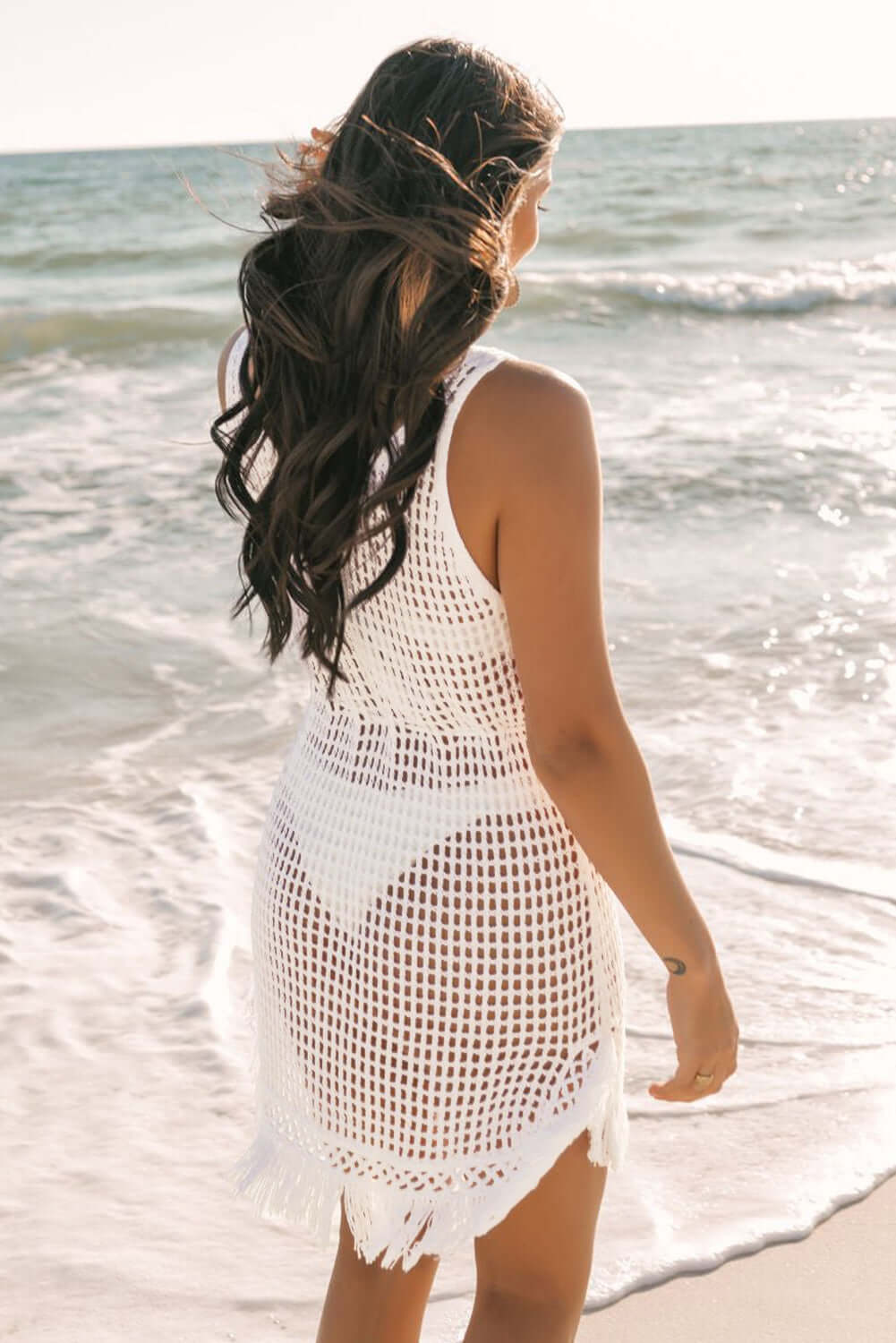 Model wearing a white crochet fishnet fringe hem beach cover up by the ocean, showcasing boho beach style.