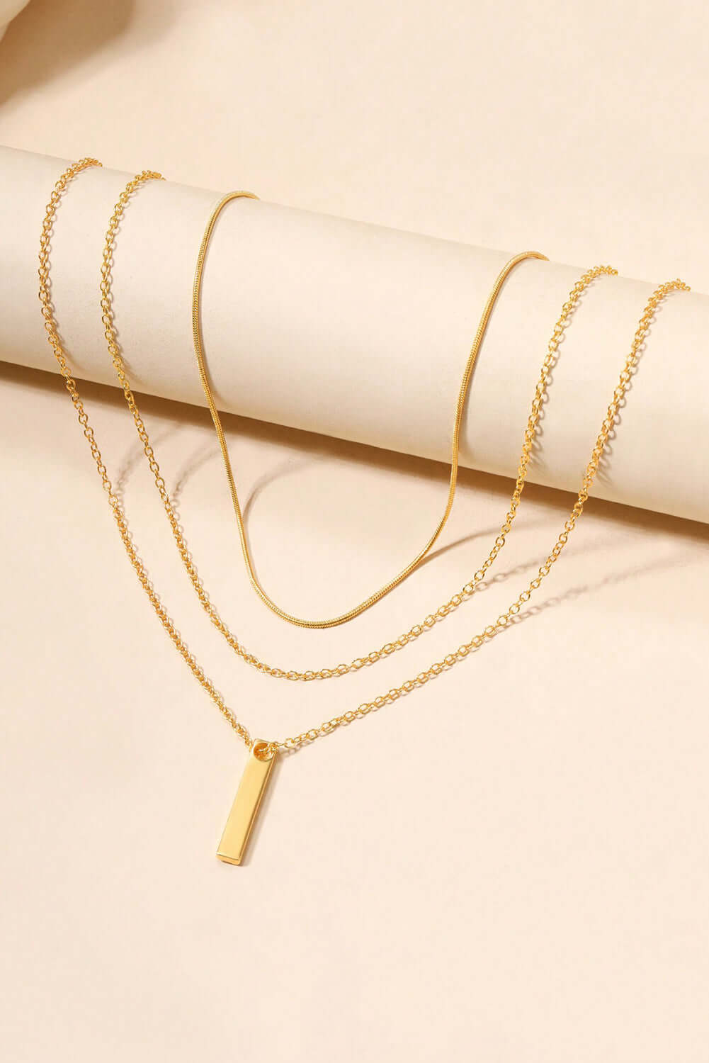 Layered adjustable gold chain necklace featuring a chic gold bar pendant, perfect for day or evening wear.