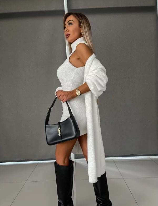 Woman wearing a white fleece-lined dress and coat, holding a black handbag.