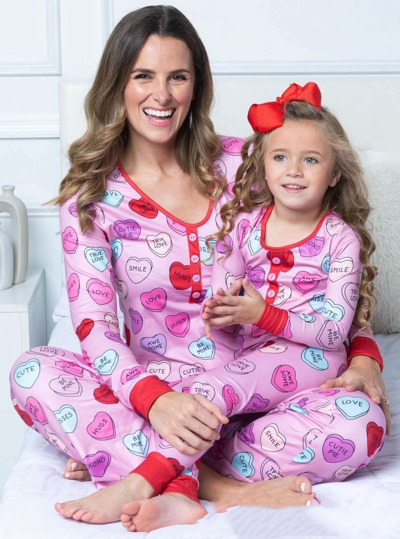 Mother and daughter in matching Valentine's Day heart-print pajamas, featuring colorful heart designs.